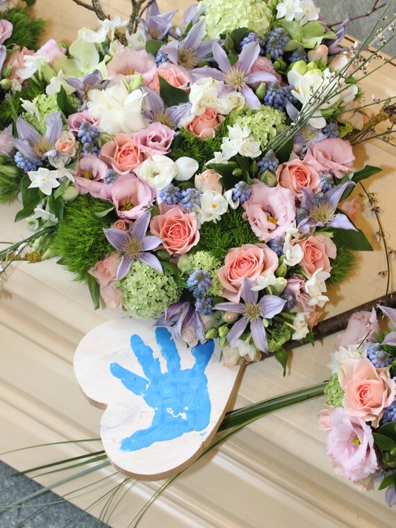 Holzsarg mit Blumengesteck aus Rosen neben Holzschild mit Abdruck Kinderhand