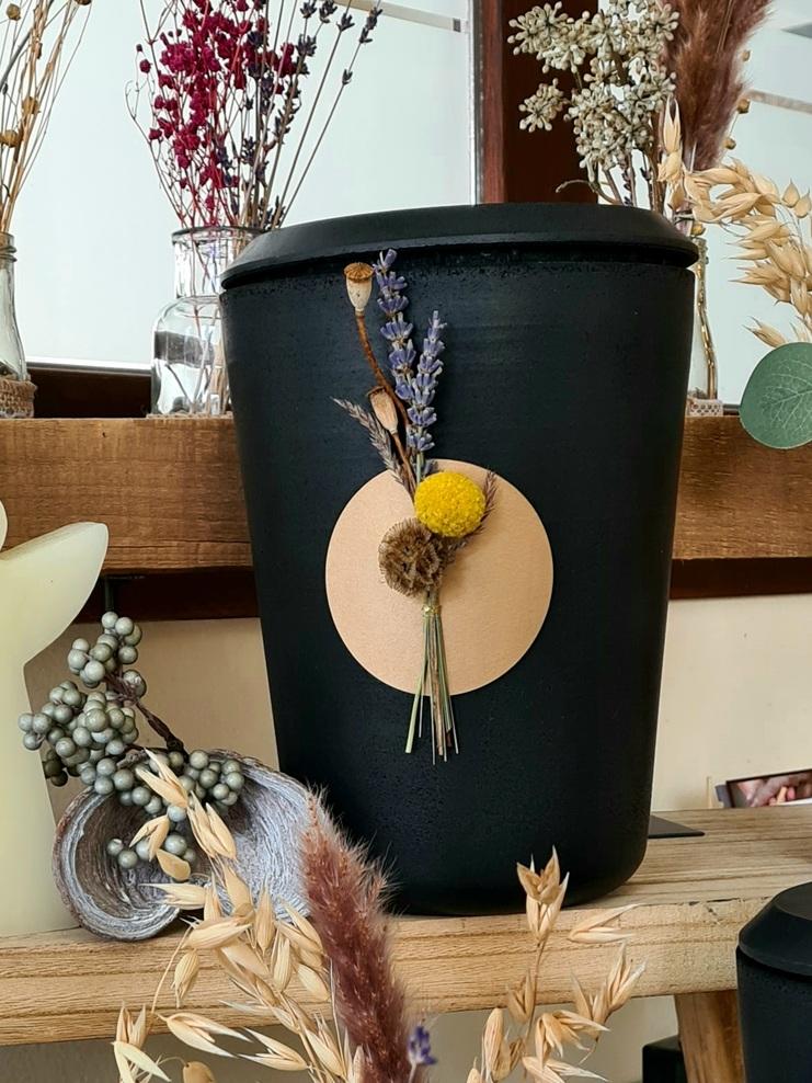 Schwarze Urne mit Blumen verziert auf Holzuntergrund