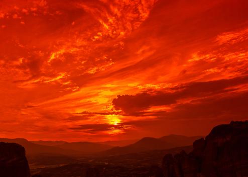 Leuchtender Sonnenuntergang mit orange-rotem Himmel über einer Gebirgslandschaft. Wolken sind sichtbar.